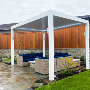 Freestanding white aluminum louvered pergola with closed roof covering a rattan sectional with navy cushions in a landscaped backyard