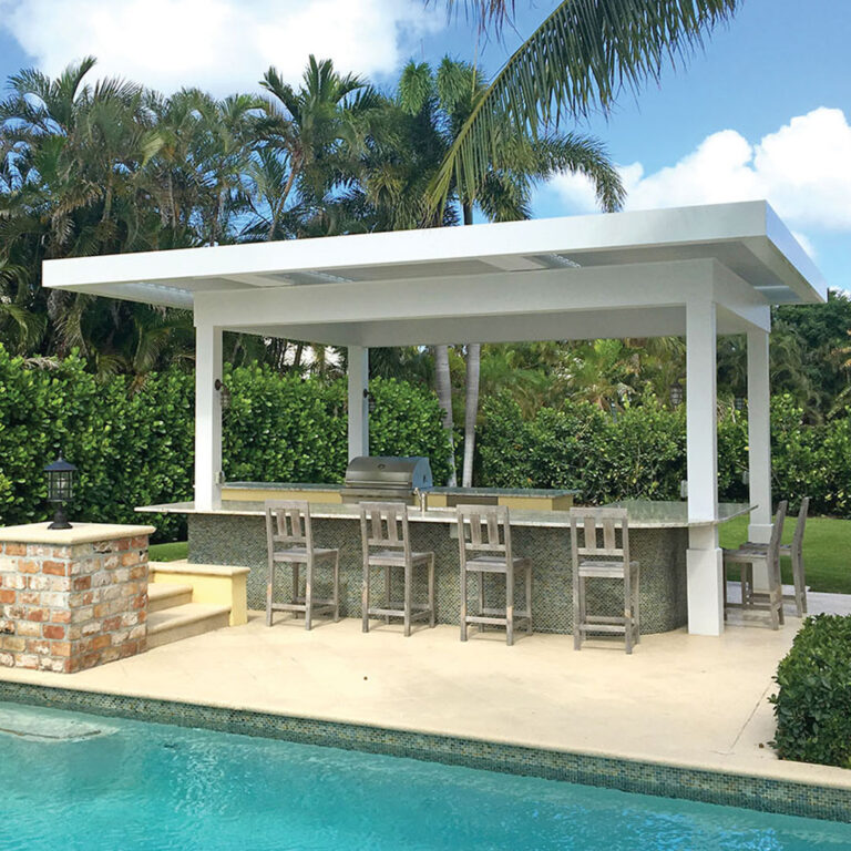 Freestanding white aluminum pergola with closed louvers sheltering a full outdoor bar with bar stools, grill station, and stone countertop beside a pool