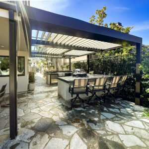 Aluminum pergola with open adjustable louvers lets sunlight through onto a stone patio with outdoor kitchen and bar seating