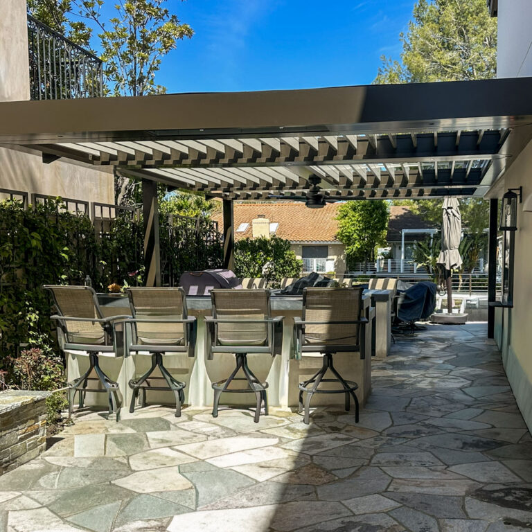 Aluminum louvered pergola with a ceiling fan and mounted heaters shades a flagstone patio with bar seating and grill