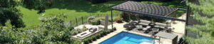 Aerial view of an aluminum louvered pergola with closed roof shading a lounge seating area beside a backyard swimming pool